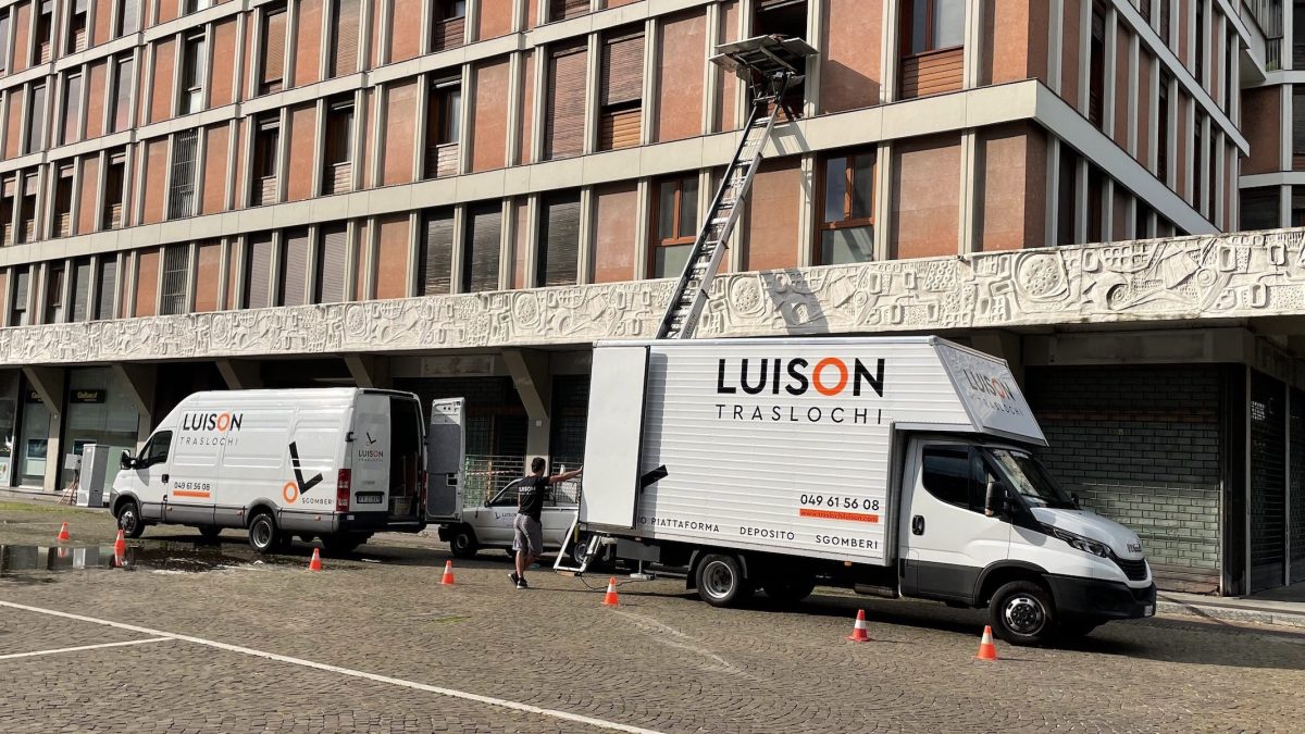 Mezzi di Traslochi Luison in strada, con la piattaforma aerea estesa verso un piano alto e i coni che delimitano l'area di carico